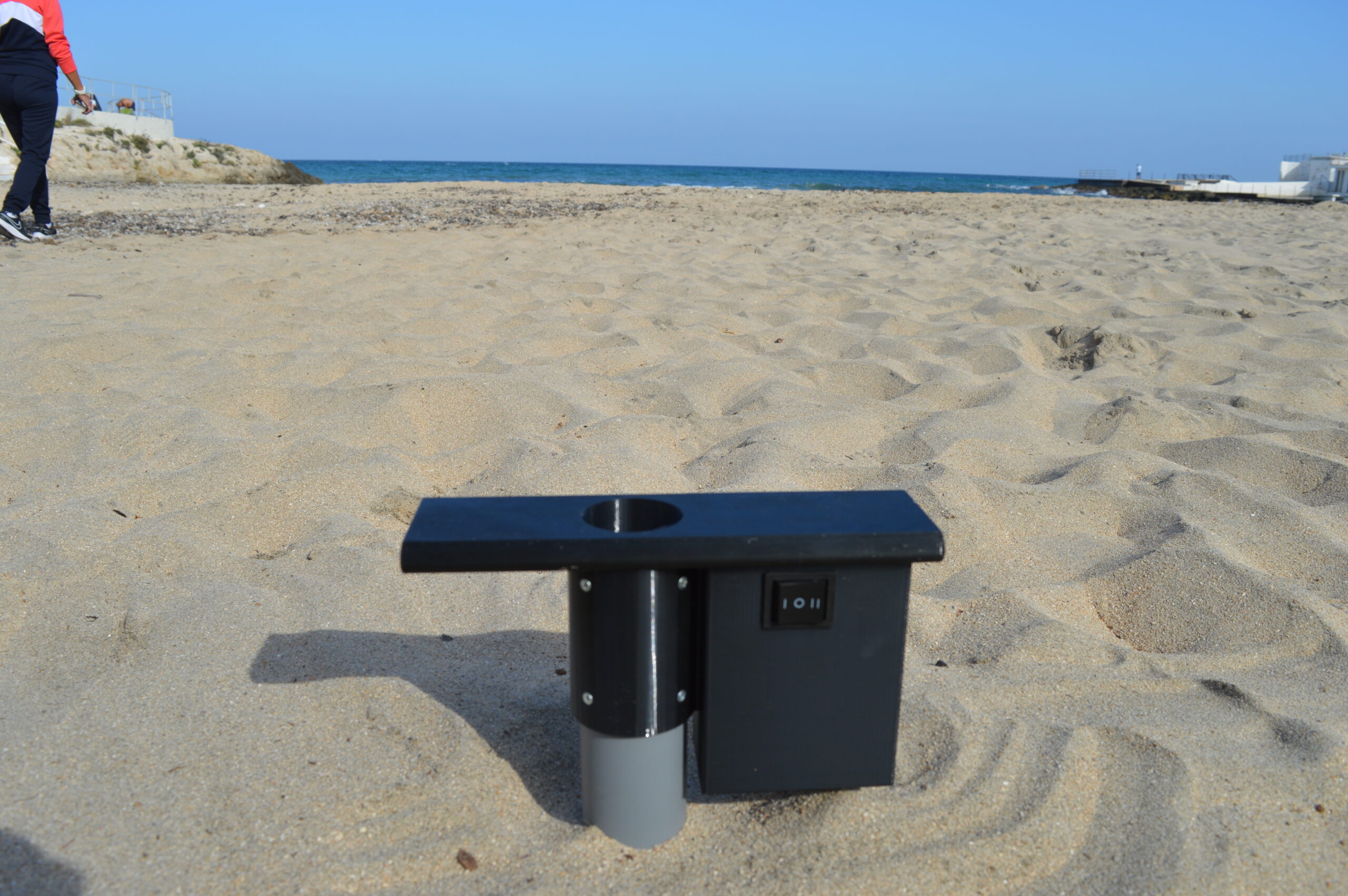 Fissaggio ombrellone con trivella elettrica su spiaggia ventosa